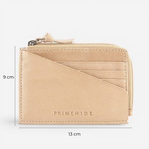 Op de afbeelding: Een beige leren portemonnee met ritssluiting en meerdere kaartsleuven. De portemonnee is 13 cm breed en 9 cm hoog. De merknaam "PRIMEHIDE" is op de voorkant in reli&euml;f aangebracht. De portemonnee is gemaakt van glad, getextureerd leer.