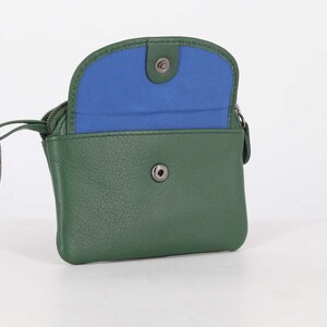 May include: A forest green leather coin purse with a snap button closure and a vibrant blue interior lining. The accessory features a metal key ring attached to the side zipper pull, providing a functional design for carrying small essentials.