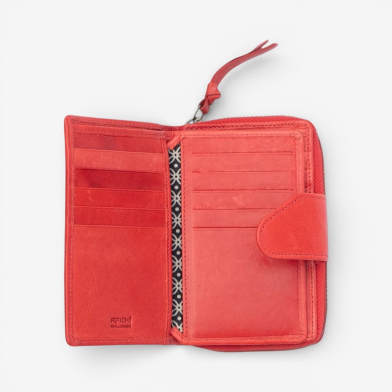 May include: Open red leather wallet with multiple card slots, a zip closure, and a wrist strap. The interior features a patterned fabric divider. The wallet is designed with RFID protection.