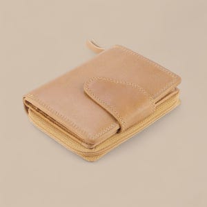 May include: A light tan leather wallet featuring a wrap-around zipper closure and a front flap secured with a snap button. The wallet has visible stitching along the edges and a smooth, matte finish, showcasing a compact and functional design.