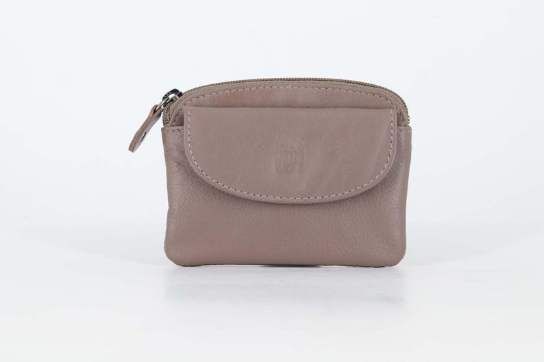May include: A taupe leather coin purse featuring a top zipper closure and a front flap pocket with a snap button. The small rectangular pouch has a smooth texture and a metal zipper pull, providing a compact storage solution for small items.