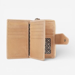 May include: Open tan leather wallet with multiple card slots, a zipped compartment, and a snap closure. The interior features a patterned fabric. The wallet is designed with RFID protection.