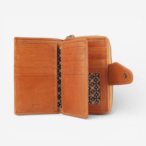May include: Open, tan leather wallet with multiple card slots and a zippered compartment. The interior features a patterned fabric lining. The wallet has a snap closure and the text "RFID REAL LEATHER" is visible.