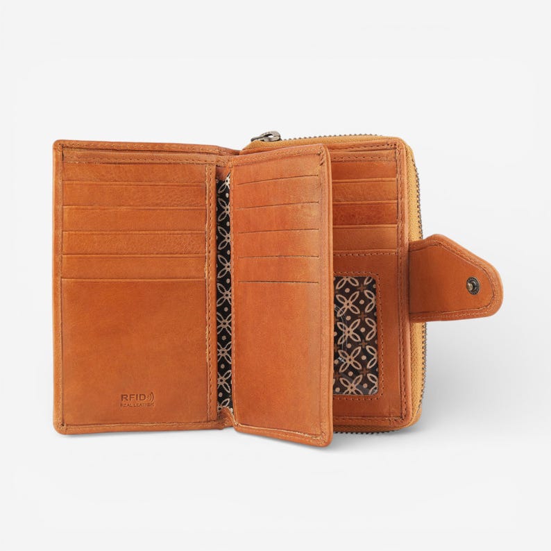 May include: Open, tan leather wallet with multiple card slots and a zippered compartment. The interior features a patterned fabric lining. The wallet has a snap closure and the text "RFID REAL LEATHER" is visible.