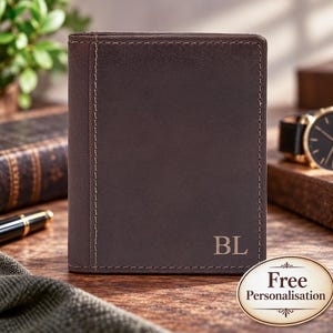 May include: A dark brown leather wallet featuring vertical stitching along the left side and the embossed initials BL in the bottom right corner. The wallet has a smooth, matte finish and a rectangular shape with clean, straight edges.