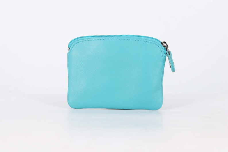 May include: A small, rectangular turquoise coin purse featuring a smooth leather-like texture and a matching turquoise zipper closure along the top edge. The pouch has rounded corners and a simple, clean design with a silver-toned metal zipper pull.