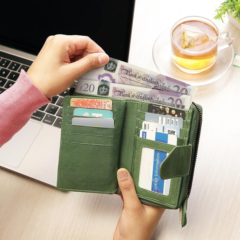 May include: A green leather bi-fold wallet, open to display credit cards and several Bank of England &pound;20 notes. The wallet has a zip closure and multiple compartments. A cup of tea is in the background.