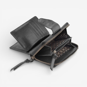 May include: Black leather wallet, open to display card slots and a zipped coin compartment. The interior lining features a patterned design. The wallet has a zip closure and a leather pull tab.