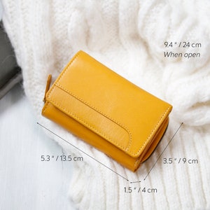 Yellow leather wallet placed on a white knit fabric, with dimensions marked as 5.3 inches / 13.5 cm in length, 3.5 inches / 9 cm in height, 1.5 inches / 4 cm in width, and 9.4 inches / 24 cm when open.