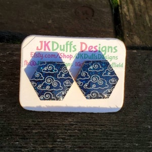 May include: Two hexagonal resin earrings with a blue glitter background and a white cloud design. The earrings are on a white card with the text "JK Duffs Designs" and the website address "Etsy.com/Shop/JKDuffsDesigns".