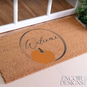 May include: A brown coir doormat with the text "Welcome" in a circle with a stylized pumpkin in the center.
