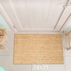 May include: A brown coir doormat with the text "24x35" printed on the bottom. The doormat is in front of a white door with a silver door handle.