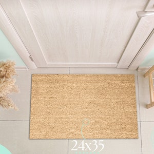 May include: A rectangular doormat made of natural fibers, measuring 24x35 inches, lies in front of a door. The mat is a light brown color and has a textured surface. The image also shows a pair of beige heels on a shoe rack.