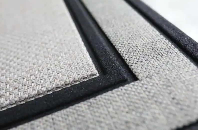 K&ouml;nnte beinhalten: Nahaufnahme eines gewebten Platzsets mit schwarzem Rand. Das Platzset hat eine hellbeige Farbe und eine strukturierte Oberfl&auml;che. Der Rand ist einfarbig schwarz.