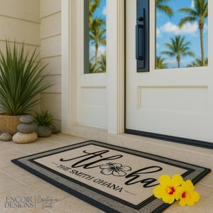 May include: A rectangular doormat with the word "Aloha" in cursive, a hibiscus flower, and "The Smith Ohana" in a serif font. The mat has a beige center, a gray border, and a black edge. Two yellow flowers are on the right.