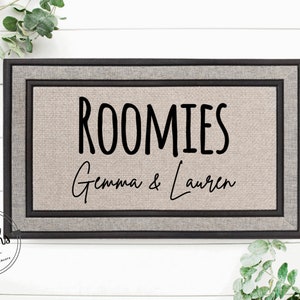 May include: A brown doormat with a black border and the text "ROOMIES Gemma & Lauren" in black.