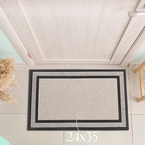 May include: A beige doormat with a black and gray border. The doormat is 24 inches by 35 inches. The doormat is in front of a closed white door.
