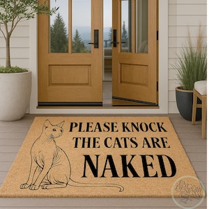 May include: A rectangular doormat made of natural coir fiber. It features a black graphic of a cat and the text "PLEASE KNOCK THE CATS ARE NAKED". The mat is placed in front of a wooden door.
