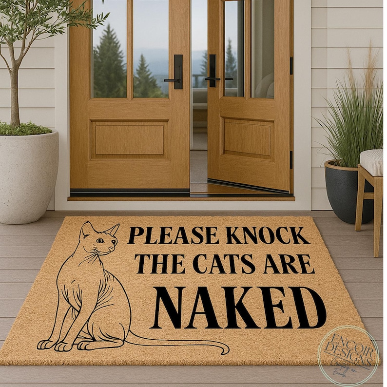 May include: A rectangular doormat made of natural coir fiber. It features a black graphic of a cat and the text "PLEASE KNOCK THE CATS ARE NAKED". The mat is placed in front of a wooden door.