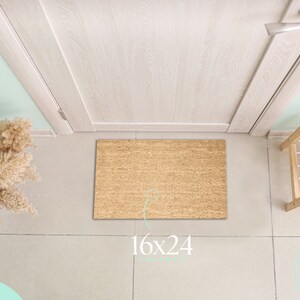 May include: A rectangular coir doormat, measuring 16x24 inches, sits in front of a light-colored door. The mat is made of natural fibers. A shoe rack with beige heels is to the right. The door is light wood.