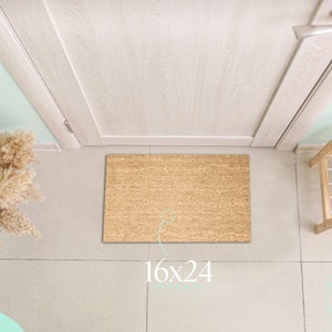 May include: A brown coir doormat with the text "16x24" printed on it. The doormat is placed in front of a white door with a silver door handle. The doormat is in a hallway with light beige tiled flooring.