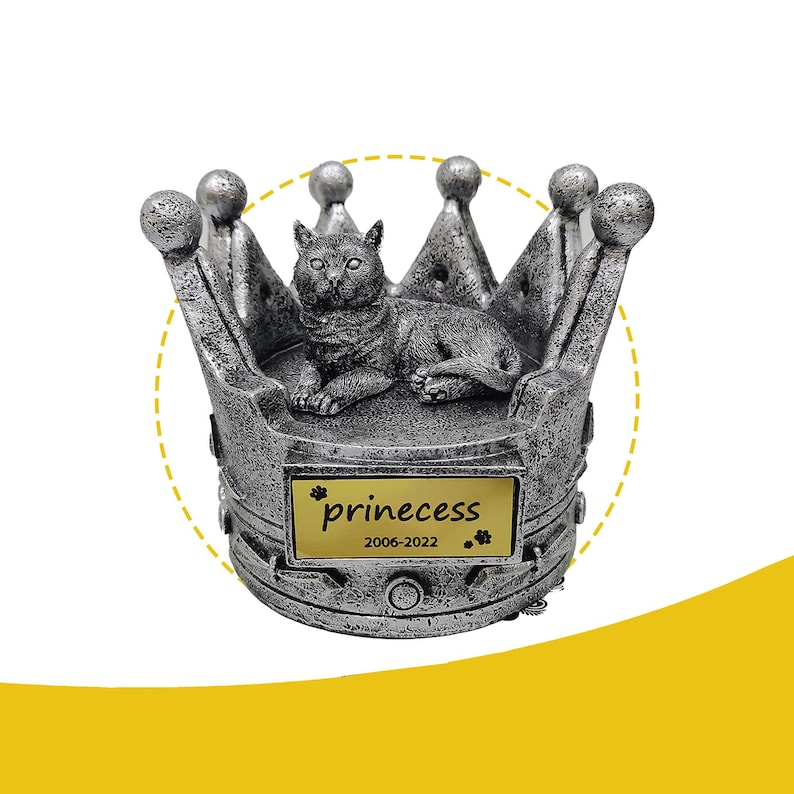 May include: Silver crown shaped pet urn with a cat figurine on top. The urn has a gold plaque with the inscription "prinecess 2006-2022".