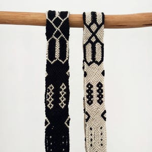 Peut inclure: Deux bandes de tissu tissées présentant des motifs géométriques complexes en noir et blanc cassé. Une bande est principalement noire avec des détails blanc cassé, tandis que l'autre est principalement blanc cassé avec des détails noirs.