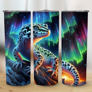 May include: A stainless steel tumbler with a colorful aurora borealis design and a gecko lizard. The gecko is perched on a rock with its tail curled around the bottom of the tumbler.