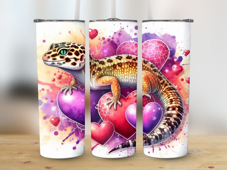 May include: A white stainless steel tumbler with a colorful watercolor design featuring a gecko lizard on a heart. The background is a mix of pink, purple, and yellow with hearts and sparkles.