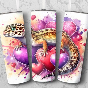 May include: A white tumbler with a colorful watercolor design featuring a leopard gecko and hearts. The gecko is perched on a large purple heart with smaller hearts scattered around it.