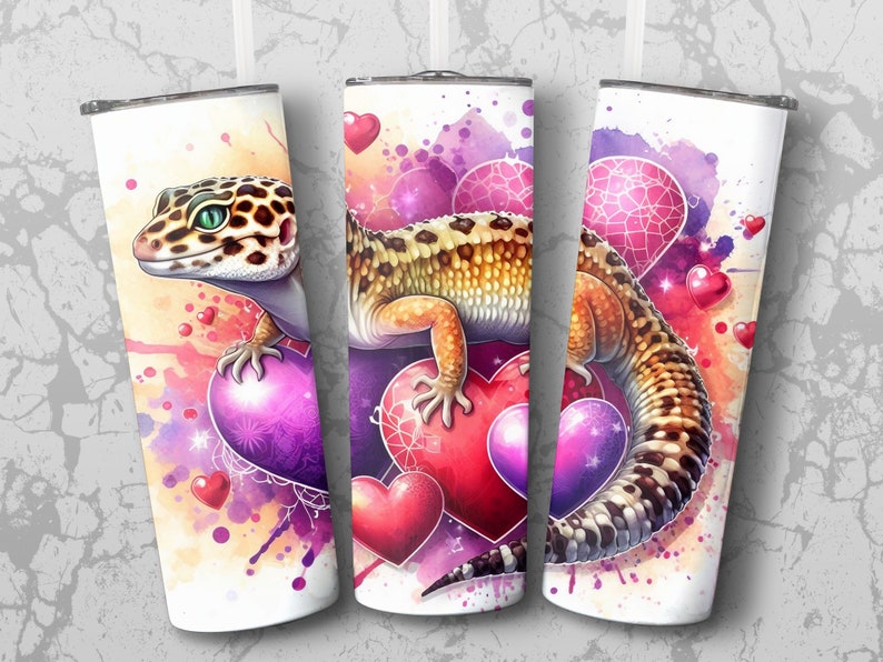 May include: A white tumbler with a colorful watercolor design featuring a leopard gecko and hearts. The gecko is perched on a large purple heart with smaller hearts scattered around it.