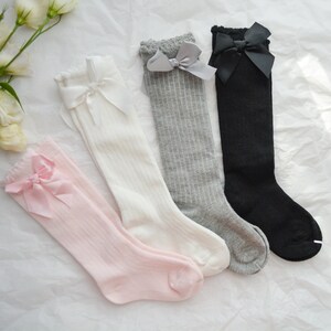 Peut inclure: Quatre paires de chaussettes hautes avec des n&oelig;uds. Les chaussettes sont en rose, blanc, gris et noir.