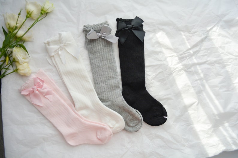 Peut inclure: Quatre paires de chaussettes hautes avec des n&oelig;uds. Les chaussettes sont en rose, blanc, gris et noir.