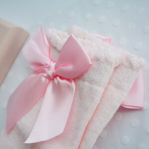 Peut inclure: Une paire de chaussettes pour b&eacute;b&eacute; roses avec un n&oelig;ud en satin rose. Les chaussettes sont en tissu doux et tricot&eacute;.