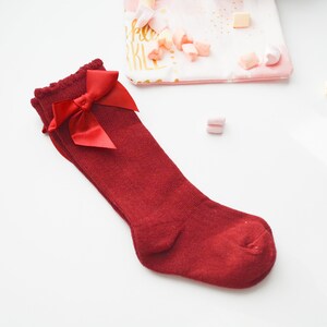 Peut inclure: Chaussettes rouges montant au genou avec un n&oelig;ud en satin rouge sur le dessus.