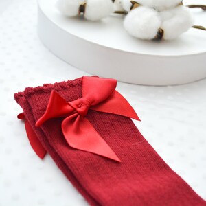Peut inclure: Chaussettes rouges montant au genou avec un grand n&oelig;ud en satin rouge.