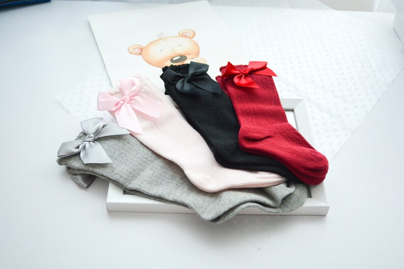 Peut inclure: Quatre paires de chaussettes hautes avec des n&oelig;uds. Les chaussettes sont en gris, rose, noir et rouge.