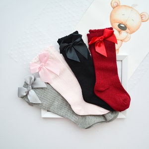 Peut inclure: Quatre paires de chaussettes hautes avec des n&oelig;uds. Les chaussettes sont grises, roses, noires et rouges. Les n&oelig;uds sont de couleurs assorties.