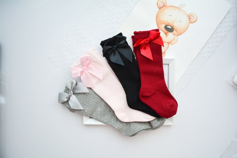Peut inclure: Quatre paires de chaussettes hautes avec des n&oelig;uds. Les chaussettes sont grises, roses, noires et rouges. Les n&oelig;uds sont de couleurs assorties.