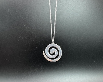 May include: A silver-colored pendant necklace featuring a spiral design. The pendant is suspended from a delicate chain. The necklace is displayed against a dark background, highlighting the bright, reflective metal.