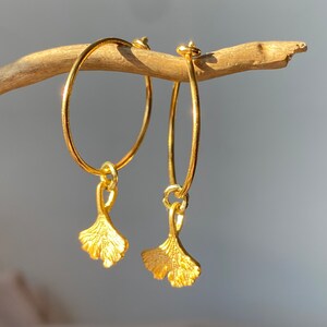 Puede incluir: Aretes de aro dorados con un dije de hoja de ginkgo colgante. Los aretes son simples y elegantes, perfectos para el uso diario.