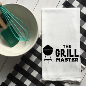 May include: White kitchen towel with black text that reads "The Grill Master" and a black silhouette of a grill.