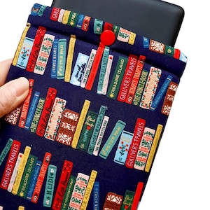 May include: A navy blue fabric book sleeve with a pattern of colorful book spines. The sleeve has a red button closure and is designed to hold a tablet or e-reader.