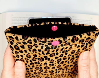May include: A rectangular fabric sleeve featuring a tan and black leopard print pattern. The opening is secured with a single bright pink plastic snap button centered on the front flap. The interior lining of the sleeve is solid black fabric.