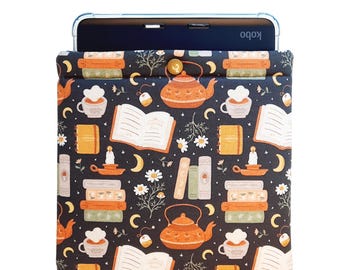 Puede incluir: Una funda para lector electrónico Kobo de color azul marino con un patrón caprichoso de libros, teteras, tazas de té, velas y lunas. El diseño incluye la palabra "NOTES" en pequeños cuadernos naranjas. La funda está diseñada para guardar un lector electrónico.