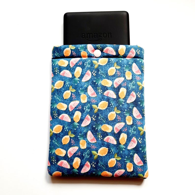 May include: A blue fabric Kindle sleeve with a pattern of lemons and watermelon slices. The top of the sleeve is closed with a white button. A black Kindle device with the Amazon logo is visible.