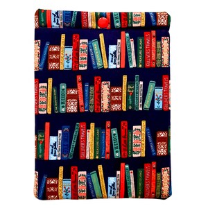 May include: A blue fabric book sleeve with a red button closure. The fabric is printed with a pattern of colorful books on a bookshelf. The titles of the books are visible, including "Gulliver's Travels", "Heidi", "Treasure Island", and "Jack and Jill".