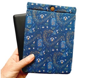 May include: A blue e-reader sleeve with a pattern of fireflies, jars, and foliage. The sleeve has a button closure and holds a black e-reader. The design features yellow and white accents.