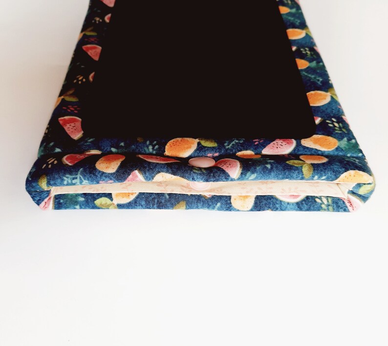 May include: A navy blue fabric case with a black interior. The case is decorated with a colorful pattern of watermelon and orange slices. A pink button secures the case closed. The case is likely for a tablet or e-reader.