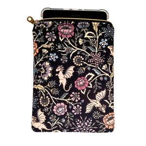 May include: A black zippered tablet sleeve with a floral and dragon pattern. The design features pink, peach, and blue flowers with cream-colored dragons. A gold zipper secures the top, and a phone is visible inside.